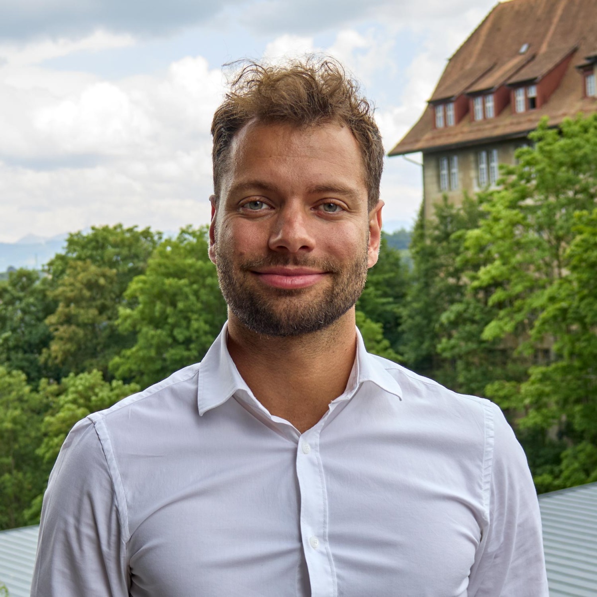 Porträtfoto von Renato Forni. Er trägt ein weisses Hemd und steht vor einem Gebäude.