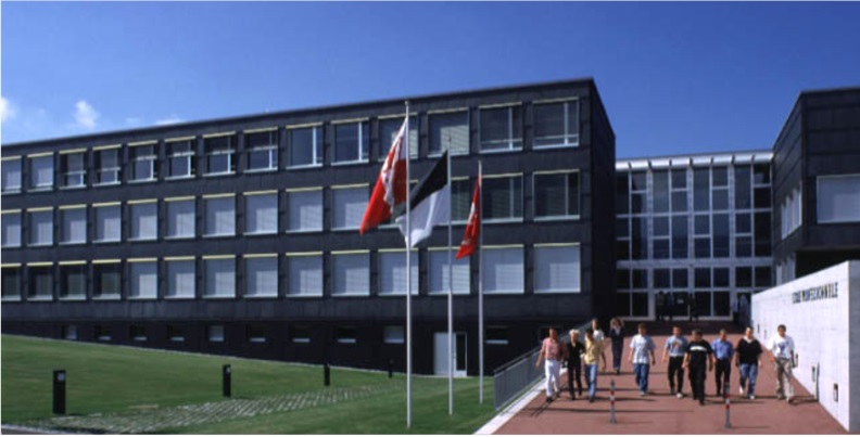Bild vergrößern Drei Flaggen vor dem EPAC-Gebäude mit gehenden Studierenden