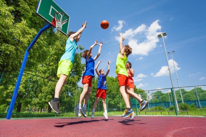 Cinq enfants jouent au basketball sur un terrain aménagée avec un panier vert