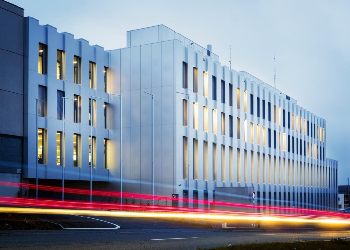Bild vergrößern Gebäude mit vielen beleuchteten Fenstern und Scheinwerferspuren im Vordergrund
